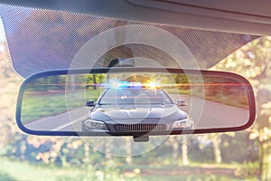 View on rear mirror of a car. Police car with lights and siren is chasing you