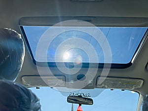 View from the rear passenger seat of an open sunroof looking up to sky on a sunny day