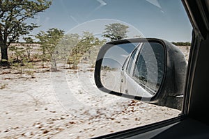 View in rear view mirror while driving through arid dry landscape in Etosha national park Namibia