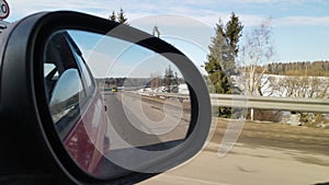 View in the rear view side mirror of a auto, driving a red car