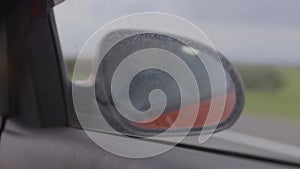 View in the rear view side mirror of a auto, driving a red car