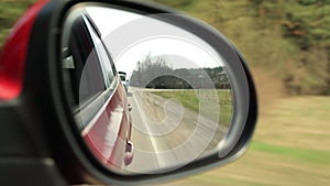 View in the rear view side mirror of a auto, driving a red car along the track