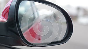 View in the rear view side mirror of a auto, driving a red car along the track