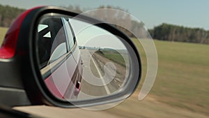 View in the rear view side mirror of a auto, driving a red car along the track