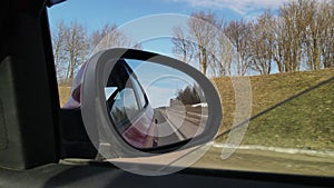 View in the rear view side mirror of a auto, driving a red car along the track