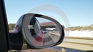 View in the rear view side mirror of a auto, driving a red car along the track