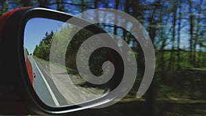 View in the rear view side mirror of a auto, driving a red car along the track