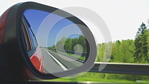 View in the rear view side mirror of a auto, driving a red car along the track