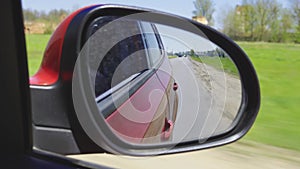 View in the rear view side mirror of a auto, driving a red car along the track