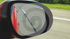 View in the rear view side mirror of a auto, driving a red car along the track