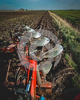 View through the rear window of a five furrow plough at work behind a red tractor.