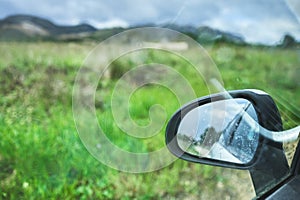 View of a rearview mirror of a car in a green grassy field