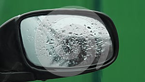 View of the rearview mirror from the car from the interior. Rain drips on the glass and mirror