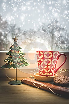 View of a red coffee cup and Christmas decoration on a window with snowy background