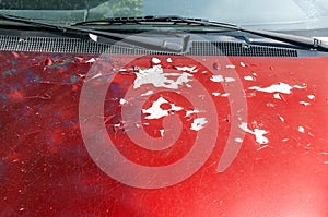 View at red color car hood with damaged paint with cracks and peeling scratched spots