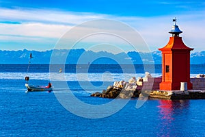 View of the red lighthouse on a pier, a fisherman on a boat and the beautiful mountain range on the horizon, Piran, Slovenia