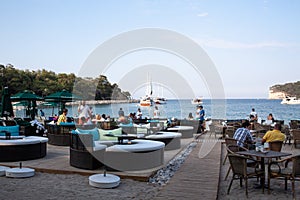 View of restaurant or cafe in Moon Light park in Kemer, Turkey. People on the beach. Tables and chairs near sea harbor