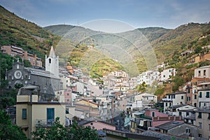 View of Riomaggiore and church of St. Giovanni Battista, Cinque Terre before the sunset along the mountaines