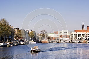 View on river Amstel in Amsterdam, capital of the Netherlands, with a boat, blue sky, trees and buildings