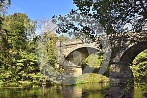 Leafy River Scene with Arches of Old Stone Bridge photo