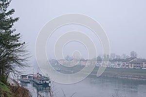 View of the river and city surrounded by fog in winter. Pleasure boat. Pavia. Italy. Lombardy