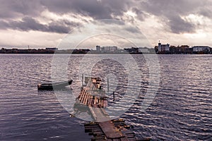 View of the river with a lonely fishing boat moored to an old wooden pier. Vintage style