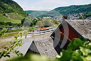 View of the river Mosel with tourist ship, green hills with vineyard and houses of small village