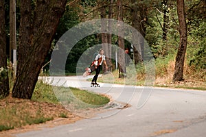 View of road along which young woman rides on skateboard with wakeboard in her hand