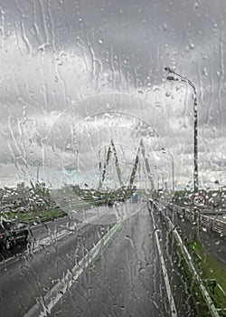 View of a road over the cable-stayed bridge in rainy weather through the glass flooded with water