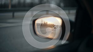 View of the road in the rearview mirror of a car at sunset