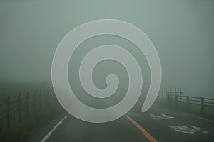 View of roadway and fence full of white fog while driving through local road on rainy and bad weather day on mount Aso area