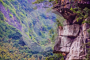 View of rock along side a sheer cliff face on a mountain and blurred trees on a mountain