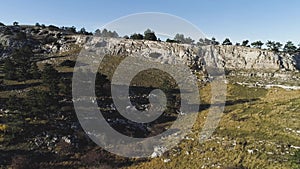 View of rocky hill with trees. Shot. Top view of yellow field with rocky outcrops and green trees. Blue clear sky over