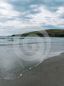 View of Rosscarbery pier from Warren Beach, southern coast of Ireland. Waves on a sandy beach. The Atlantic in cloudy weather.