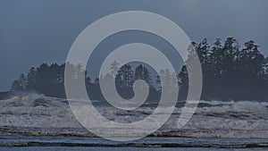 Rough Pacific Ocean on the coast of Long Beach with waves and the silhouettes of trees near Tofino on Vancouver Island, Canada.