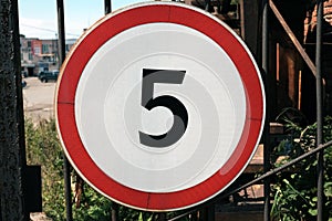 View of round white road sign with red border indicating speed limit of 5 km h, on industrial metal mesh fence