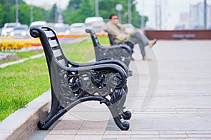 View on a row of benches in a city park with a man sitting in blur