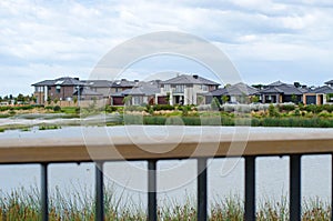 View of a row of modern suburban houses by a lake over the fence of a viewing platform. Concept of real estate development
