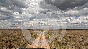 View from a safari jeep on the African savannah. Panorama of fields, small hills and a jeep driving in front and leaving clouds of