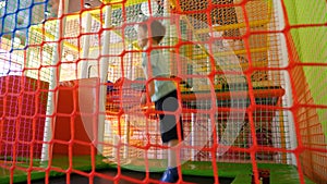 View through the safety net on cheerful little boy jumping and playing on trampoline at indoor playground