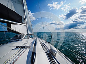 View on a sailboat bow of white sailing yacht on a lake during sailing in a summer sunny day