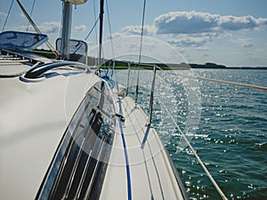 View on a sailboat bow of white sailing yacht on a lake during sailing in a summer sunny day