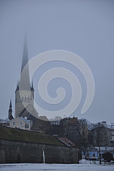 View of Saint Olaf Church in Tallinn, Estonia behind the brick city wall in light haze on cloudy weather