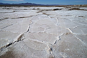 A view of salt desert field with crystallized dry salt formations and mountains on the background