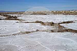 A view of salt desert field with crystallized dry salt formations and mountains on the background