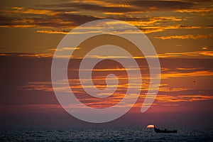 view of sea boat against large sun disk rising from behind sea