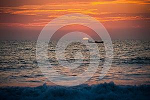 view of sea boat against large sun disk rising from behind sea