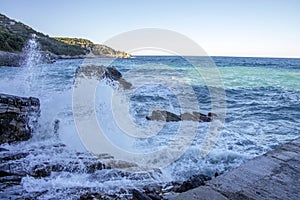 View of the sea and the hills from the pier. Splashes of water from the sea waves crashing against the stone cliffs