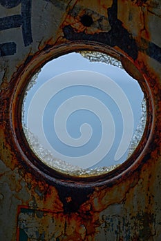 View of sea through the round window of an old, rusted ships hull