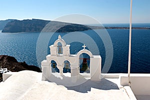 View of sea surface through traditional Greek white church arch with cross and bells in Oia village of Cyclades Island, Santorini,